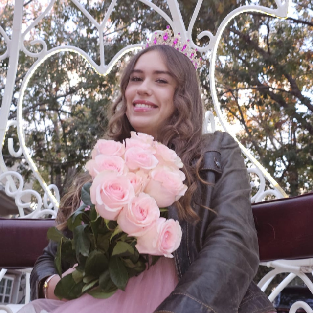 Nathali sonriendo sentada con ramo de rosas en el carruaje
